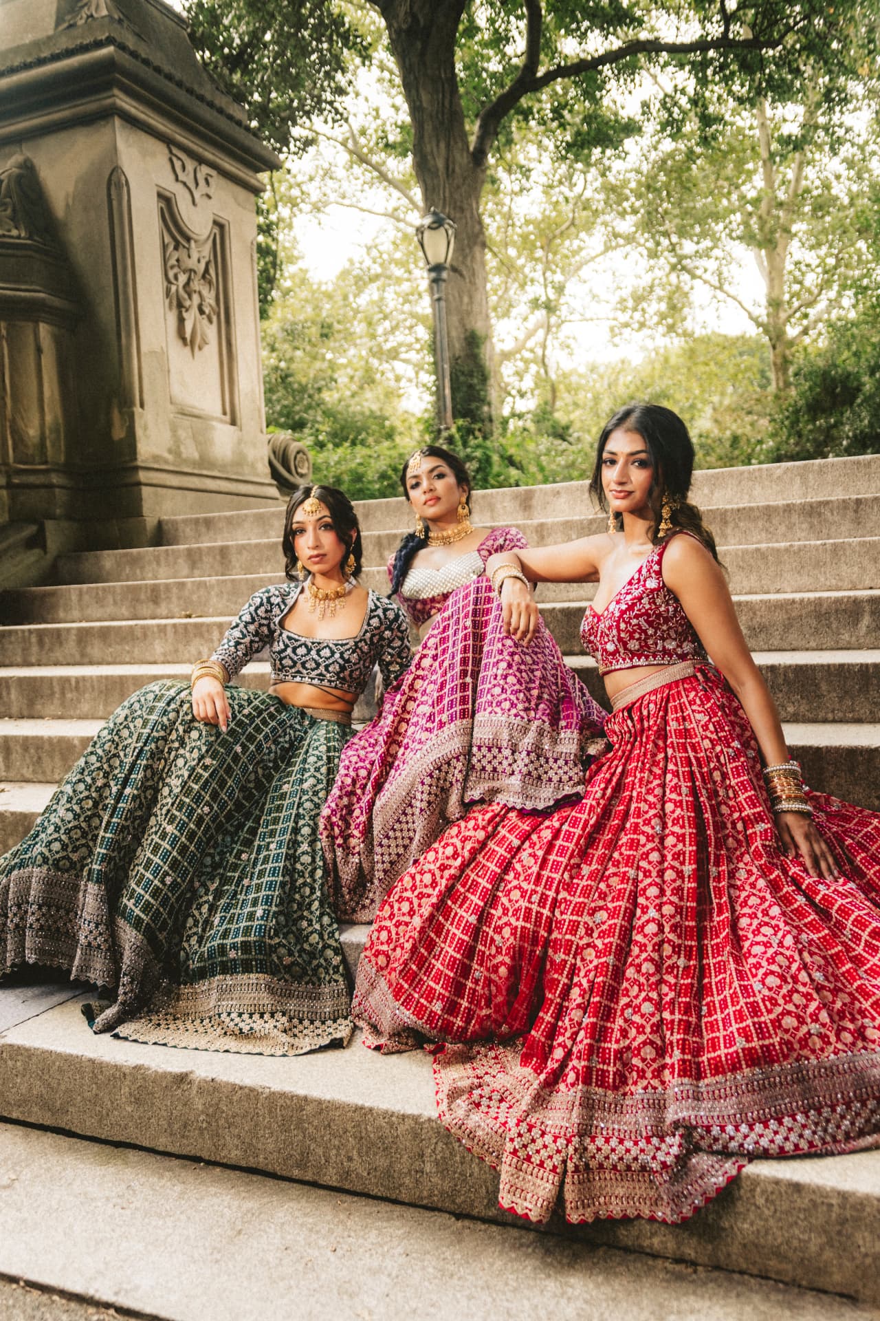 Three models seated together on the steps in Rangrez lehengas