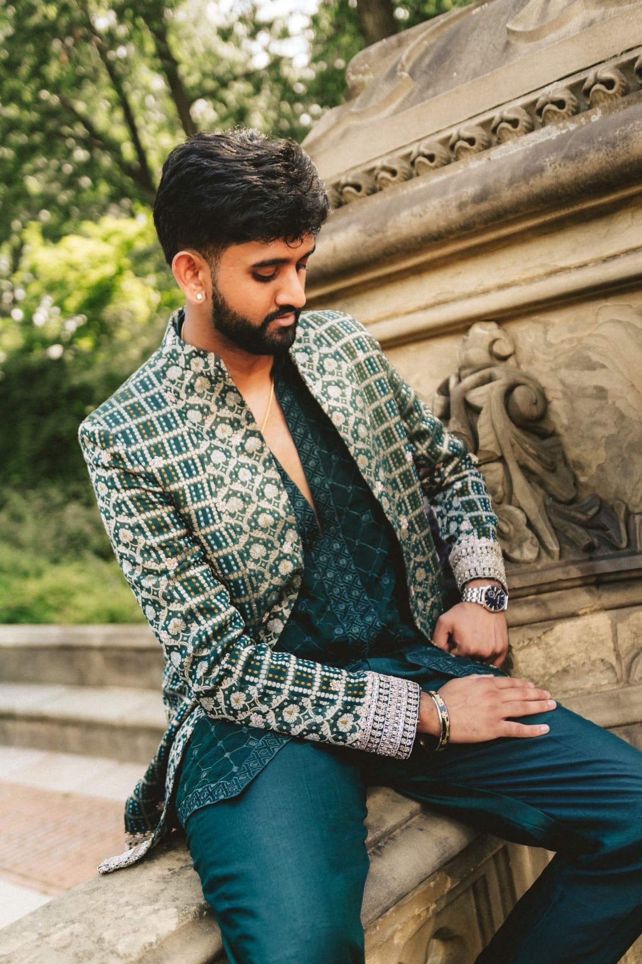 Model seated on carved stone in an emerald bandhani jacket set with silver embroidery